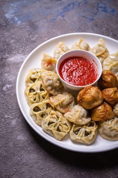 A delicious assortment of Uzbek dumplings with meat, pumpkin, and greens served on a plate with a side of red sauce