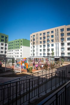 Modern apartment buildings with a courtyard playground. Contemporary design, large windows, balconies. Playground with swings, slide, climbing frame.