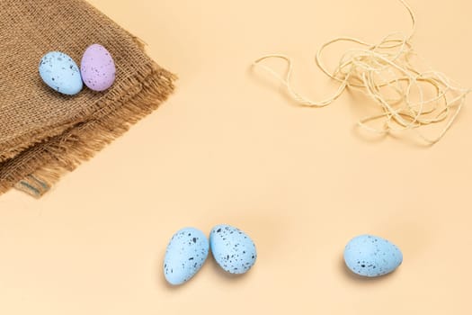 Colored Easter eggs with a sackcloth bag and a rope on the beige background. Top view.