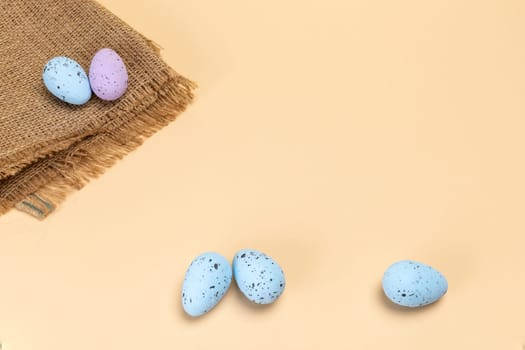 Colored Easter eggs with a sackcloth bag on the beige background. Top view with a copy space.