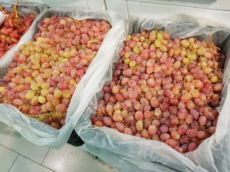 Lots of fresh ripe red grapes in containers on the market, close-up.