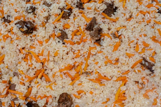 Close-up view of Eastern tasty food background. Traditional Asian culinary dish - pilaf. Ingredients: rice with slices of meat, fat and vegetables (carrot, garlic), spices- popular recipe.
