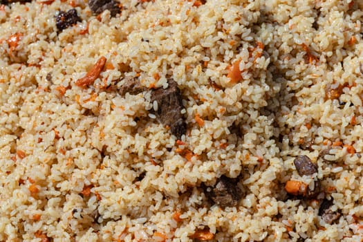 Traditional Eastern culinary dish - pilaf. Close-up view of Asian tasty food background. Ingredients: rice with slices of meat, fat and vegetables (carrot, garlic), spices- popular recipe.