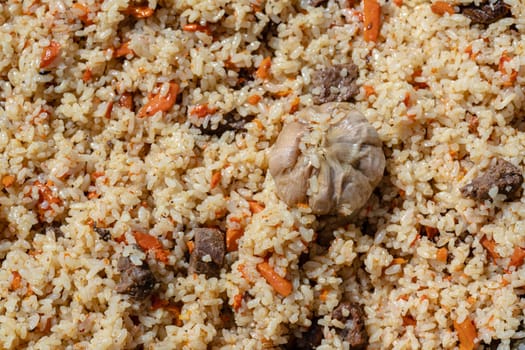 Traditional Eastern culinary dish - pilaf. Ingredients: rice with slices of meat, fat and vegetables (carrot, garlic), spices - popular recipe. Close-up view of Asian tasty food background.