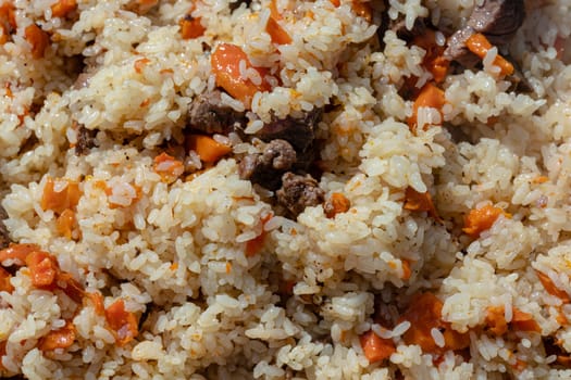 Traditional Asian culinary dish - pilaf. Close-up view of Eastern tasty food background. Ingredients: rice with slices of meat, fat and vegetables (carrot, garlic), spices - popular recipe.