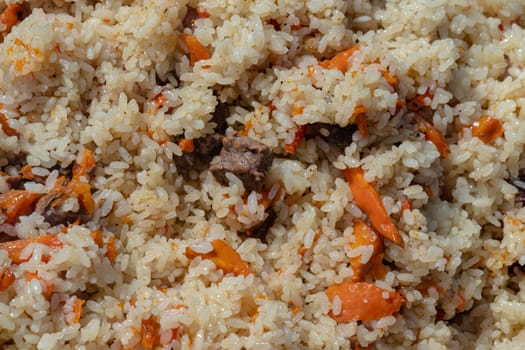 Traditional Asian culinary dish - pilaf. Ingredients: rice with slices of meat, fat and vegetables (carrot, garlic), spices- popular recipe. Close-up view of Eastern tasty food background.