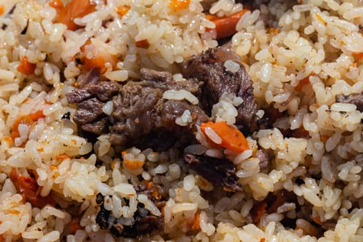 Traditional Eastern culinary dish - pilaf. Close-up view of Asian tasty food background. Ingredients: rice with slices of meat, fat and vegetables carrot, garlic, spices. Popular recipe.