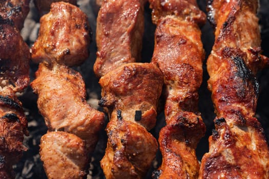 Tasty juicy pork barbecue cooking on metal skewers on outdoors charcoal grill with fragrant fire smoke. Close-up view, cooking during summer picnic. Selective focus on pieces of delicious roast meat.