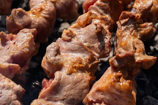 Juicy appetizing pork shish kebabs cooking on metal skewers on charcoal grill with fragrant smoke. Close-up view, selective focus on tasty pieces of roast meat. Cooking during summer picnic.
