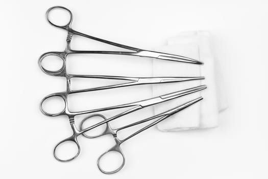 Lot of stainless surgical needle drivers lying on white sterile gauze swab. Medical instruments needle holders on white background. Healthcare and medicine concept. Flat shot, selective focus