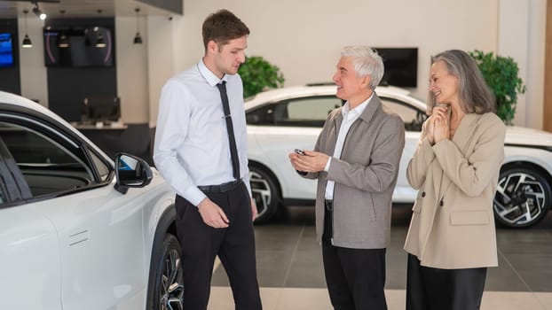 A salesman hands over the keys to a new car to an elderly Caucasian couple