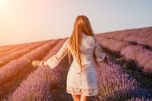 Close up portrait of young beautiful woman in a white dress and a hat is walking in the lavender field and smelling lavender bouquet.