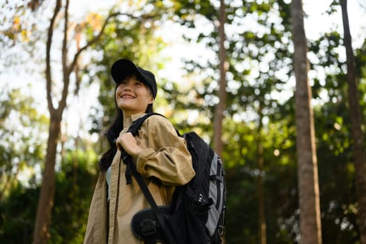 Relaxed young woman with backpack trekking in forest and enjoying nature.