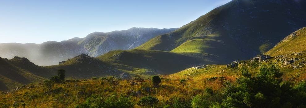 Mountain, fog and natural hill with field, blue sky and calm landscape for travel location. Nature, green and sustainable environment with earth, peace and holiday destination with conservation.