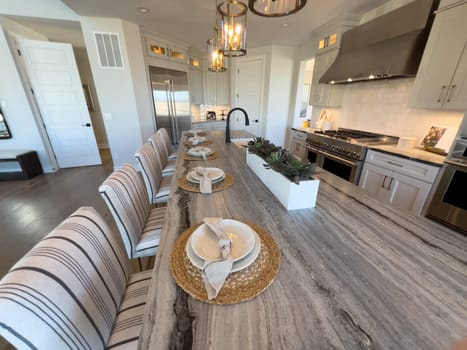 Denver, Colorado, USA-February 29, 2024-This inviting kitchen boasts a long dining table set for a family meal, with modern pendant lighting overhead and a sleek kitchen island that promises memorable gatherings and culinary adventures.