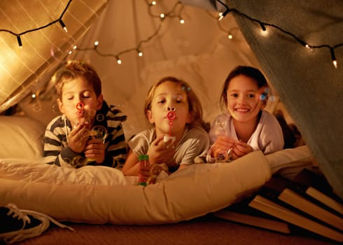 Children, fort and portrait of siblings in a bed with fun, toy and bonding while blowing bubbles at home together. Family, night and kids in a bedroom for evening games, playing or indoor camping.