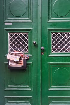 A green wood door with a mailbox attached, featuring a rectangle facade. The door handle is a fixture on this home door, mounted on a wall