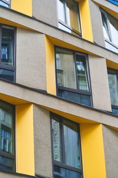 The building features a facade with numerous windows, including a standout yellow corner. The composite material structure has a rectangular shape with a rooftop, emphasizing its modern design