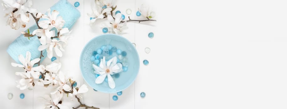 turquoise bowl with water and mother of pearl spa stones for gentle manicure in the salon with white magnolia flowers on the table,copy space, High quality photo