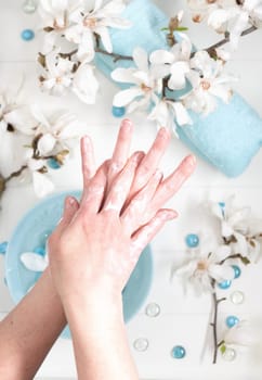 young woman doing step by step finger massage with cream in salon with cup of spring water and blue spa stones and white magnolia flowers, High quality photo