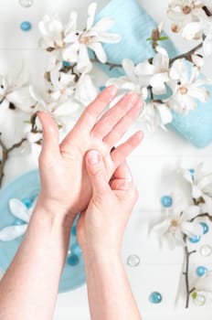 young woman doing step by step hand massage with cream in salon with cup of spring water and blue spa stones and white magnolia flowers, High quality photo