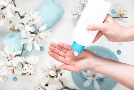 young woman doing step by step hand massage with cream in salon with cup of spring water and blue spa stones and white magnolia flowers, High quality photo