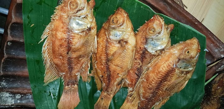 Seafood dish served on the table and plate from above with different kind of dish from fried fish barracuda, snapper, tuna jaws, and also mix of tropical vegetables and sambal or chili paste