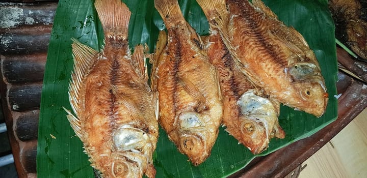 Seafood dish served on the table and plate from above with different kind of dish from fried fish barracuda, snapper, tuna jaws, and also mix of tropical vegetables and sambal or chili paste