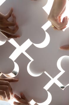 Below view of diverse corporate officer workers collaborate in office connecting puzzle pieces as partnership and teamwork concept. Unity and synergy in business idea by merging jigsaw puzzle. Concord