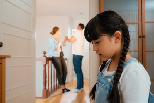 Stressed and unhappy young girl huddle in corner, cover her ears blocking sound of her parent arguing in background. Domestic violence at home and traumatic childhood develop to depression. Synchronos