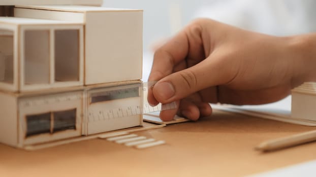 Closeup image of skilled professional engineer hand using ruler measures house model on table with blurred background. Creative design, architect design, architectural equipment concept. Immaculate.