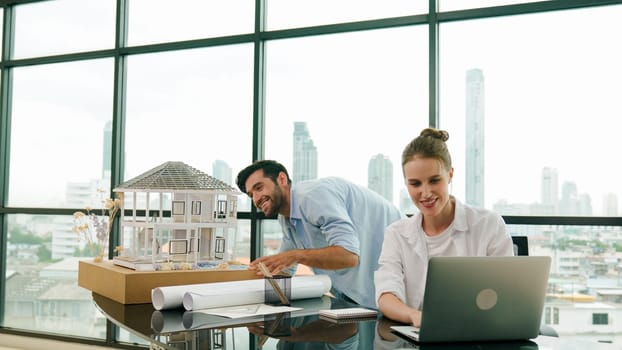 Smart architect engineer inspect house model while colleague using laptop analysis data. Professional designer team working together to design house model construction at modern office. Tracery