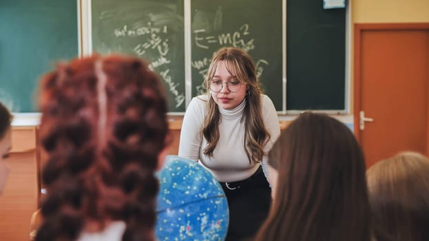 Children's education. Funny schoolchildren and their positive female teacher play fun games in creative lesson. Elementary school students laugh loudly and clap their hands together in classroom.