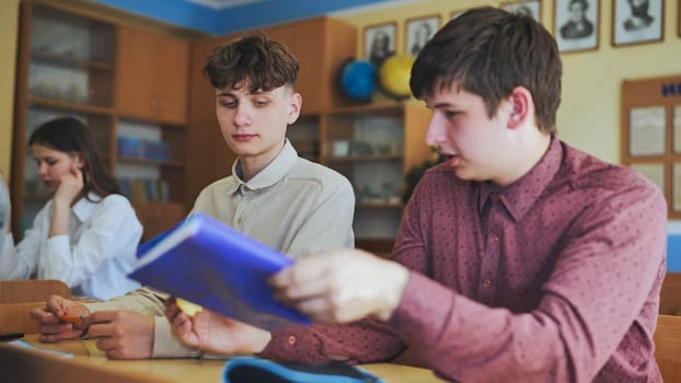 Schoolboys at a desk during class. The boy eats an apple