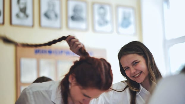 Fun schoolgirls in the classroom. Girl playing with her friend's pigtail