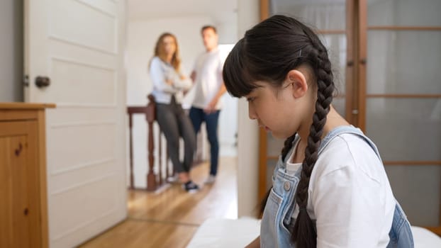 Stressed and unhappy young girl huddle in corner, cover her ears blocking sound of her parent arguing in background. Domestic violence at home and traumatic childhood develop to depression. Synchronos