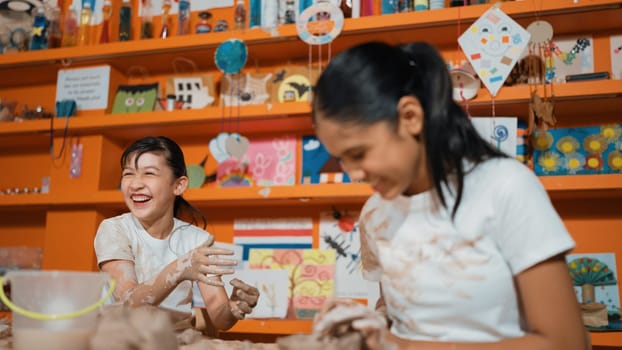 Happy multicultural girl and friend put the clay on the each other muddy shirt at art lesson. Diverse highschool student playing with clay at pottery workshop. Creative activity concept. Edification.