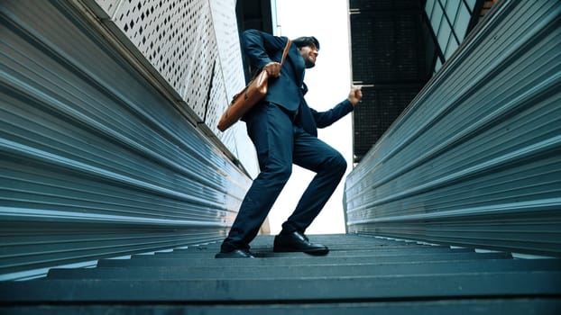 Low angle view of young smiling business man dance between building at center point. Skilled executive manager wearing suit and suitcase and moving to music. Happy investor moving to music. Exultant.