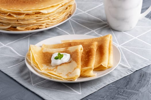 Stack of russian thin pancakes blini with fresh sour cream.