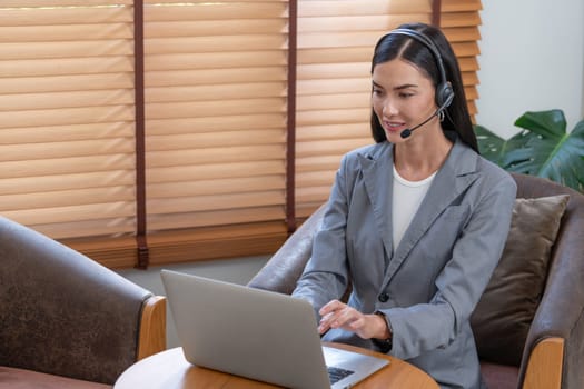 Female call center operator or customer service helpdesk staff working on workspace while talking on the headset to provide assistance for customer. Professional modern business service. Blithe