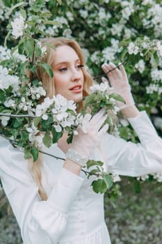 A blonde girl with long hair on a walk in a spring park. Springtime and blooming apple trees