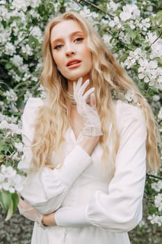 A blonde girl with long hair on a walk in a spring park. Springtime and blooming apple trees