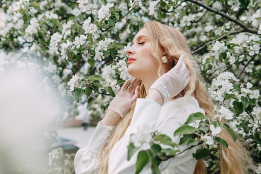 A blonde girl with long hair on a walk in a spring park. Springtime and blooming apple trees