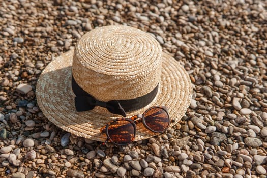 A straw hat and sunglasses on the beach. Pebbles on the seashore, close-up. The natural background.