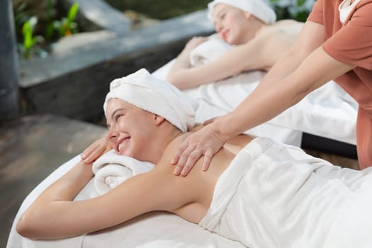 A portrait of two young attractive woman lie on bed during having back massage by a professional masseur at outdoor surrounded by peaceful natural environment. Healthy and beauty concept. Tranquility.