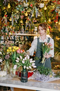 A woman in her florist shop collects bouquets of flowers. The concept of a small business. Bouquets of tulips for the holiday on March 8