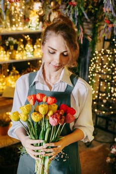 A woman in her florist shop collects bouquets of flowers. The concept of a small business. Bouquets of tulips for the holiday on March 8