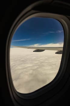 Beautiful view from the white wing of a passenger plane in the clouds against the blue sky through the porthole, side view close-up.