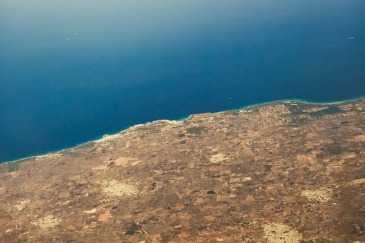 Beautiful view of the blue sea with part of the island through the airplane window in the summer during the flight, close-up side view.