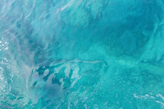 Beautiful view of blue colored water with white foam bubbles in the lower left corner on a sunny summer day, close up view from above.